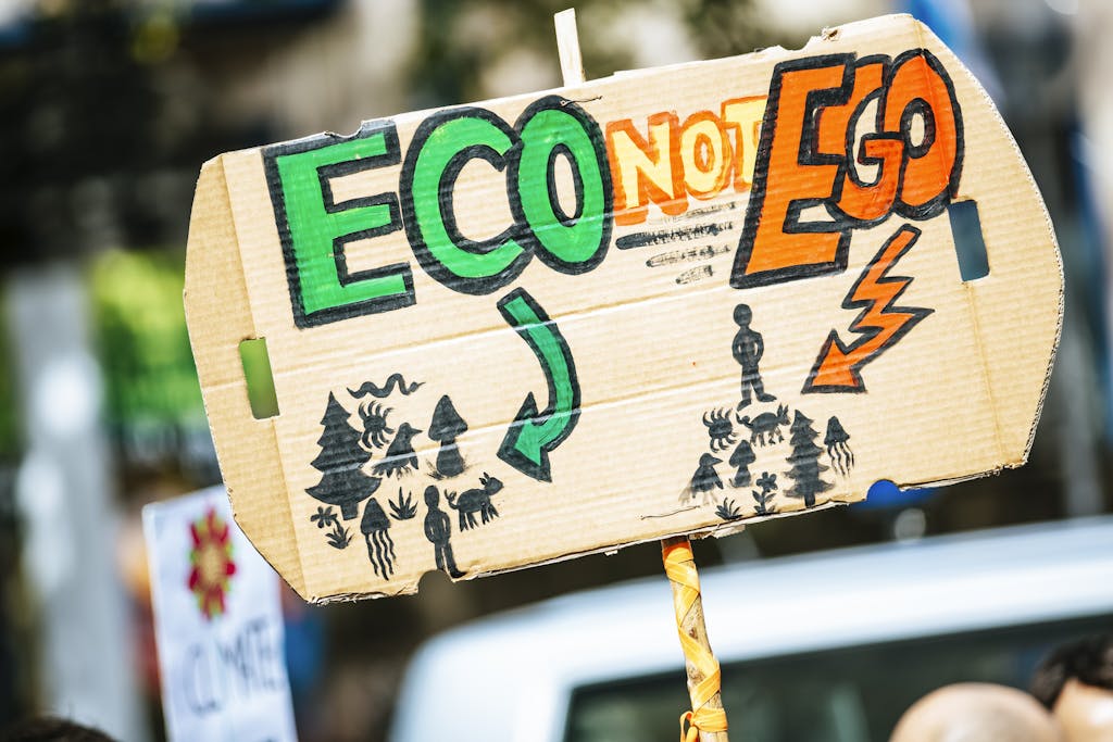 Close-up of a cardboard protest sign with 'Eco Not Ego' message at a climate rally.