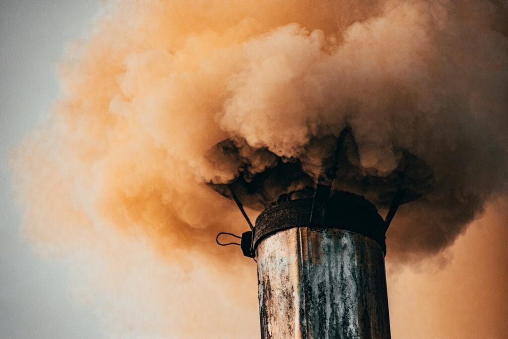 A close-up of a factory smokestack releasing thick smoke into the air, illustrating industrial pollution.