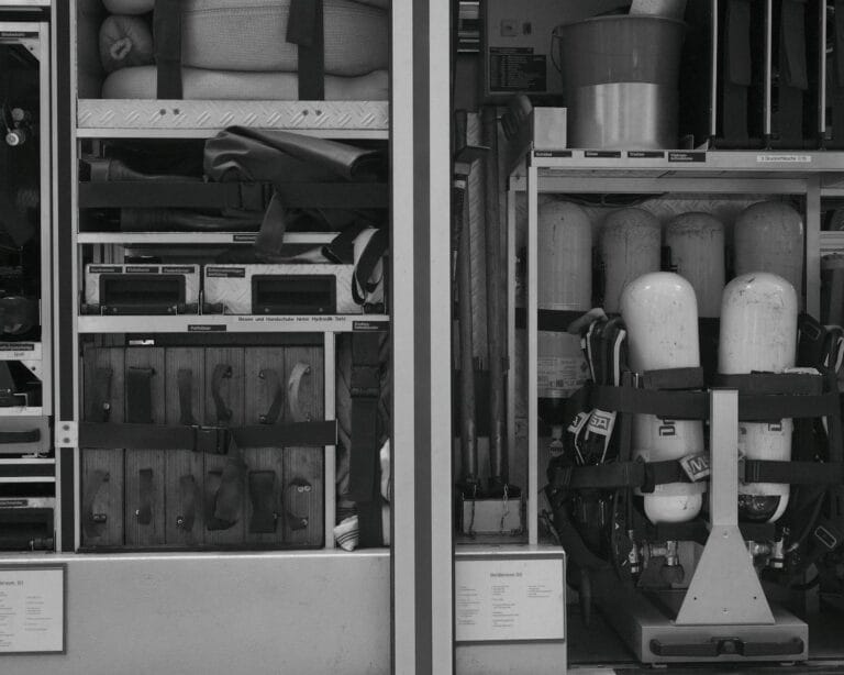 Black and white photo of firetruck equipment and rescue gear neatly organized in compartments.