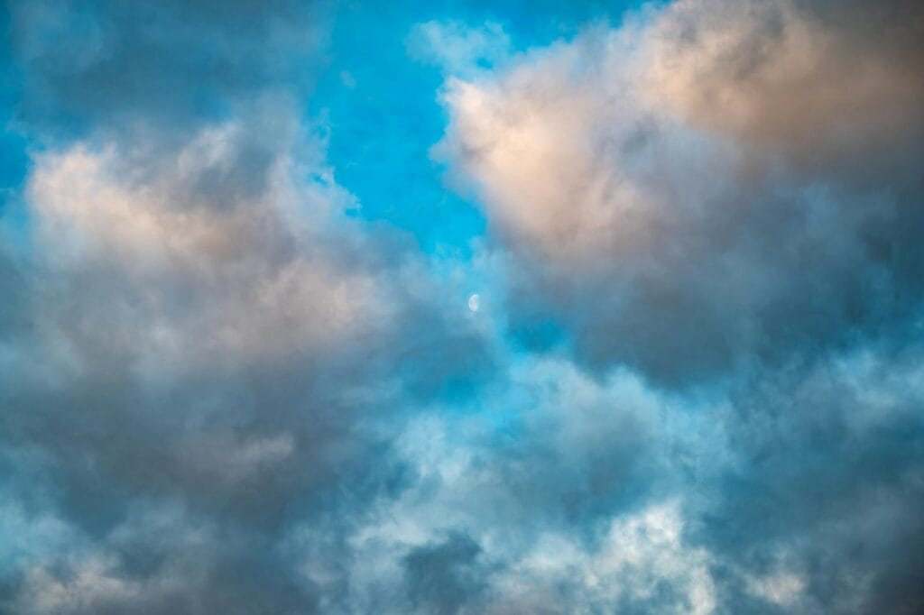 A captivating scene of clouds with gentle sunlight and the moon peeking through, perfect for sky-themed projects.