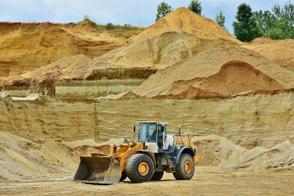 An excavator working in an open pit mine surrounded by sandy terrain and clear sky. Green company, raja ampat.