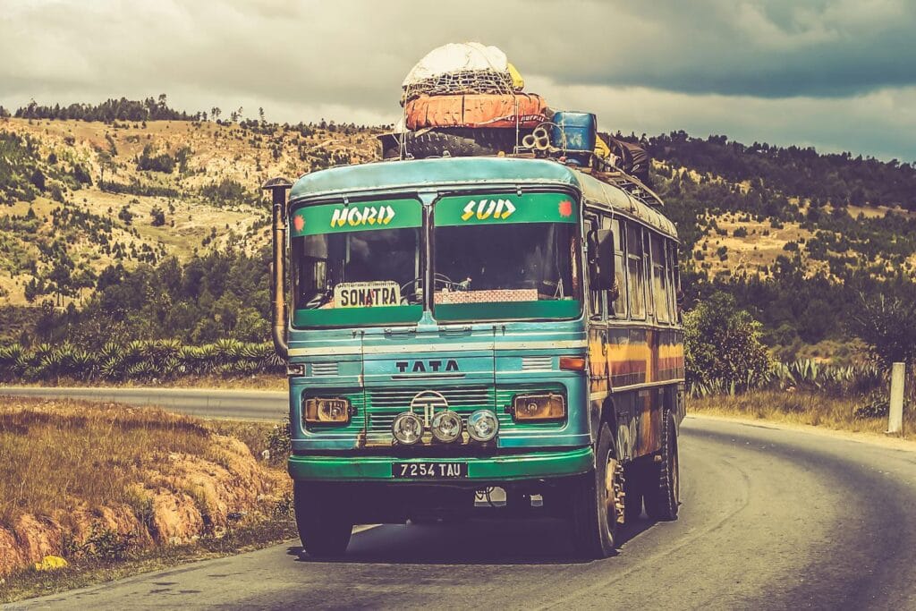 Colorful vintage bus traveling on a scenic countryside road under a cloudy sky. Public Transportation Electrification!.