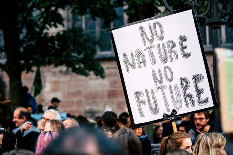 Large group of people rallying with a sign advocating for nature protection and climate action. kebijakan lingkungan. Environmental Policy